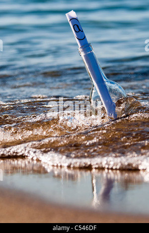 eine Flaschenpost mit einem at-Zeichen in der Brandung Stockfoto