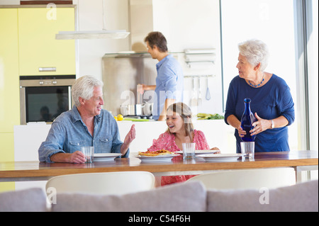 Mädchen sitzen mit ihren Eltern am Esstisch und ihr Vater Kochen im Hintergrund Stockfoto