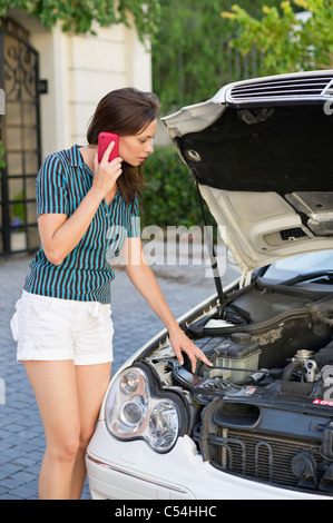Junge Frau im Gespräch über Telefon und dem kaputten Auto Standby Stockfoto