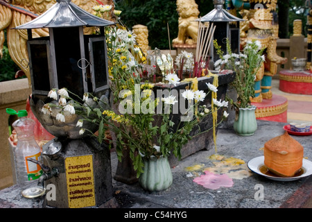 Blumen, Laternen und andere Objekte bilden eine Outdoor-Altar-Display in einem buddhistischen Tempel in Nordthailand. Stockfoto