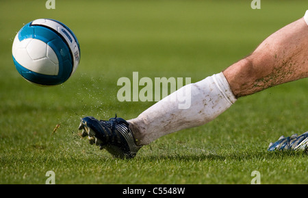 Ein Fußballer gleitet in einem Zweikampf Gras- und Wasser in die Luft zu schicken. Stockfoto