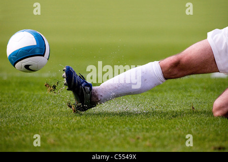 Ein Fußballer gleitet in einem Zweikampf Gras- und Wasser in die Luft zu schicken. Stockfoto