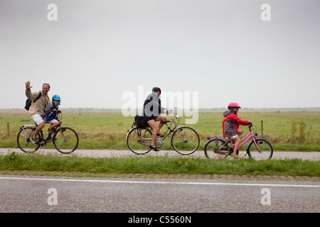 Die Niederlande, Ballum, Ameland Insel, gehört zum Wadden Sea Islands. UNESCO-Weltkulturerbe. Familie Radfahren im Regen. Stockfoto