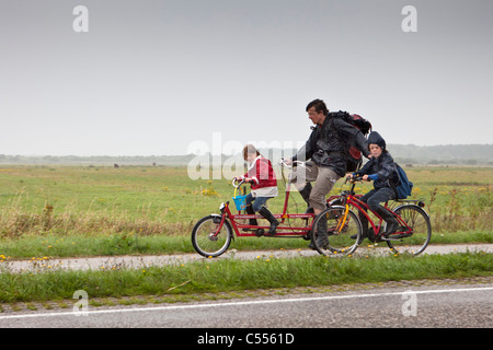 Die Niederlande, Ballum, Ameland Insel, gehört zum Wadden Sea Islands. UNESCO-Weltkulturerbe. Familie Radfahren im Regen. Stockfoto