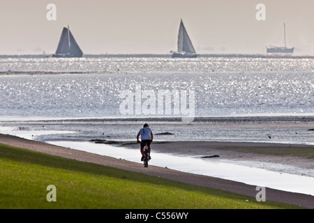 Die Niederlande, Ballum, Ameland Insel, gehört zum Wadden Sea Islands. Segelboote und Mann Radfahren am Deich Stockfoto