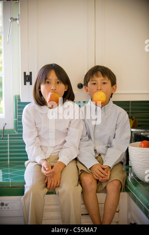 Junge und seine Schwester sitzt auf einem Küchentisch und Verzehr von Äpfeln Stockfoto