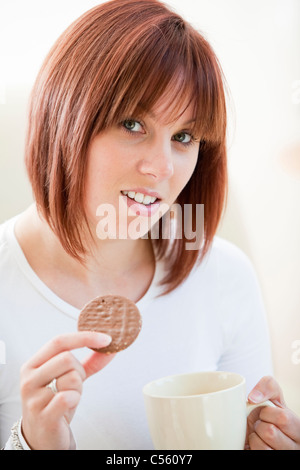 Attraktive junge Frau eine Schokolade Keks essen und trinken eine Tasse Kaffee Stockfoto