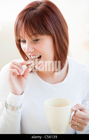 Attraktive junge Frau eine Schokolade Keks essen und trinken eine Tasse Kaffee Stockfoto