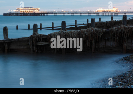 Worthing Pier und hölzernen Buhne Küstenschutzes bedeckt in Algen vom Strand im Abendlicht Stockfoto