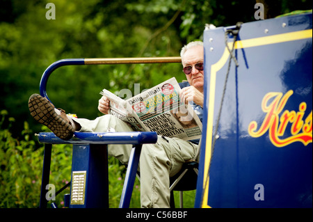 Leute, die Spaß auf dem Fluss Wey Navigationen in der Nähe von Godalming, Surrey, UK. Ein Steuermann liest der Daily Mail. Stockfoto