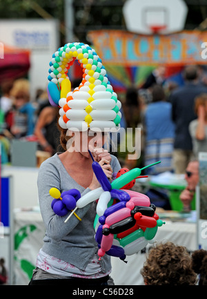 Frau mit viel Blätterteig Sprengung Ballons, verrückte Hüte auf der Patchfest Community Festival Veranstaltung in Brighton UK Stockfoto