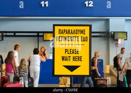 Melden Sie sich an einen Check-in-Schalter in einem griechischen Flughafen bitten Passagiere, "Bitte warten Sie hier" Stockfoto