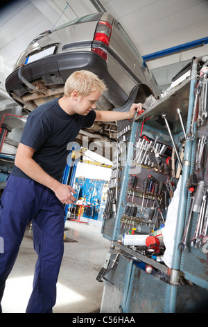 Hübscher Junge Mechaniker an der Reparatur der Werkzeuge in Autowerkstatt suchen Stockfoto