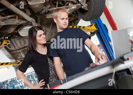 Gereizte junge Frau mit Mechaniker mit Laptop in garage Stockfoto