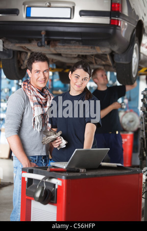 Porträt der Arbeitnehmerin mit Laptop stehen neben den Client in Garage mit Person im Hintergrund Stockfoto