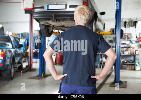 Rückansicht des Auto-Werkstatt Blick auf Auto im Auto-Reparaturwerkstatt mit Händen auf Taille Stockfoto