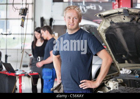 Porträt eines jungen Mechanikers in Auto-Werkstatt mit Kunden im Hintergrund Stockfoto