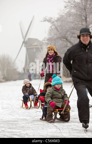 Den Niederlanden, Ankeveen. Familie Eis Schlittschuhlaufen und Rodeln vor Windmühle. Stockfoto