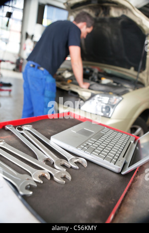 Nahaufnahme eines Laptop und Schraubenschlüssel und Mann Mechaniker arbeitet im Hintergrund Stockfoto