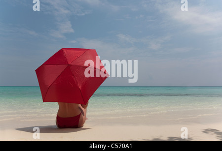 Frau sitzt unter Sonnenschirm am Strand Stockfoto