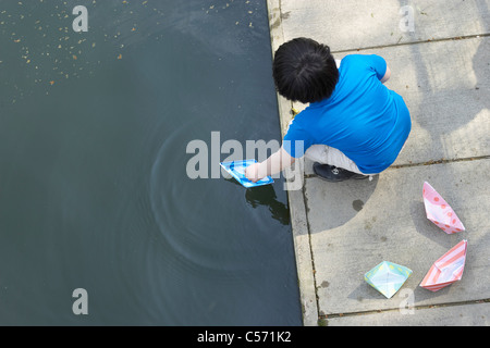 Jungen spielen mit Papier Segelschiffe in Teich Stockfoto