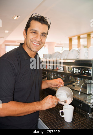 Man gießt geschäumte Milch in Kaffeetasse Stockfoto