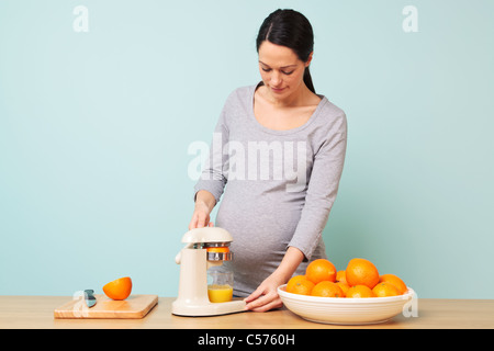 Foto von einer 32 Woche schwanger Frau in ihrer Küche frisch gepressten Orangensaft. Stockfoto