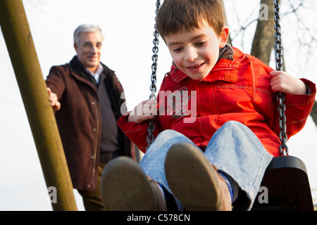Mann schob Enkel auf Schaukel im park Stockfoto