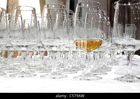leere Whiskygläser mit einem gefüllten Glas auf weißem Tischtuch Stockfoto
