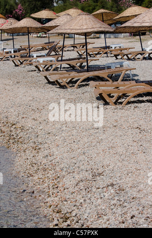 Leere Liegestühle mit Reservierung Handtücher und Sonnenschirme an einem tropischen Strand bei Sonnenaufgang Stockfoto