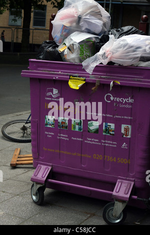 Ein Wheelie bin überfüllt mit Müll mit Teil der gedumpten Fahrrad in der Nähe Stockfoto