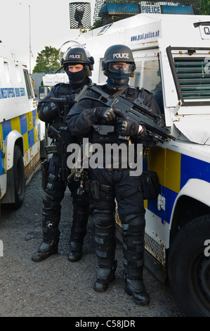 Polizisten in Kampfmontur ein Riot bewaffnet mit einem Heckler & Koch G36C automatische Maschinengewehr Stand neben einem gepanzerten Landrover Stockfoto