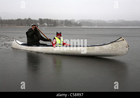 Mann und Kind sitzt in einem Kanu auf einem zugefrorenen See Stockfoto