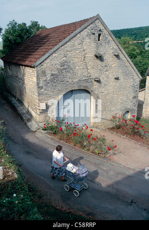 Frau Kinderwagen durch einen steinernen Granery, Dorf Chevroches Region Burgund, Frankreich. Stockfoto