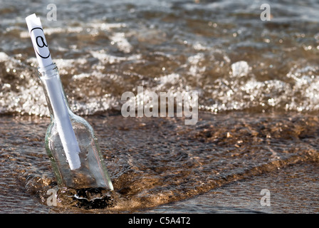 eine Flaschenpost mit einem at-Zeichen in der Brandung Stockfoto