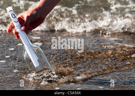 eine Flaschenpost mit einem at-Zeichen in der Brandung Stockfoto