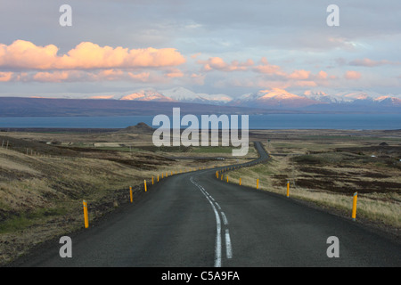 Kurvige Straße in Island mit Berge und Wolken, die von der untergehenden Sonne gemalt. Stockfoto