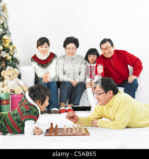 Vater und Sohn spielen Schach, Familie sitzend im Hintergrund Stockfoto