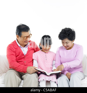 Großeltern mit Enkelin auf Sofa sitzen, Buch lesen Stockfoto