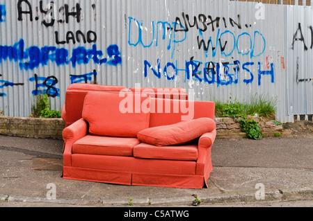 Zwei alte rote Sofas links auf einem Wanderweg neben einem Zaun mit "Kein Müll" darauf geschrieben. Stockfoto