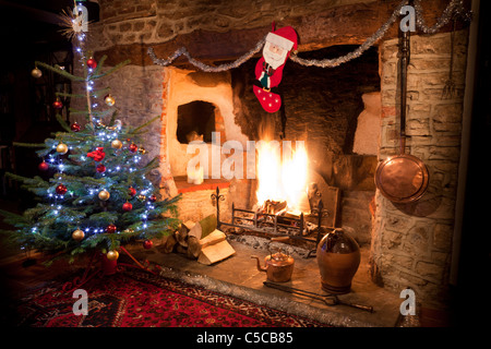 Kaminecke im alten Haus mit hoch lodernden Kaminfeuer und geschmückten Weihnachtsbaum, Bevorratung und Kupfer Wasserkocher. JMH 5161 Stockfoto