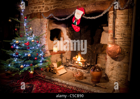 Inglenook Kamin in alten Haus mit niedrigen brennenden Feuer anmelden und dekorierten Weihnachtsbaum, Strumpf und Kupfer-Kessel. JMH5162 Stockfoto