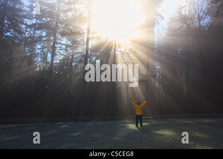 Eine Person wirft ihre Arme, die Sonne scheint durch Morgennebel und Bäume; Happy Valley, Oregon, Vereinigte Staaten von Amerika Stockfoto