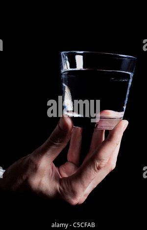 Des Mannes Hand, die ein klares Glas Wasser auf einem schwarzen Hintergrund Stockfoto