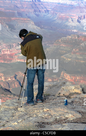 Ein Tourist richtet ein Stativ am äußersten Rand des Grand Canyon. Der Tourist kroch hinter einer Sicherheitsbarriere, sein Bild zu nehmen. Stockfoto