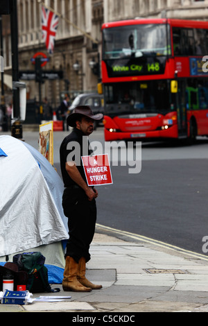 Protestler mit Plakat „Ein Hungerstreik“ an der Peace Campaign des Parliament Square / Friedenslager Brian Haw, roter Bus im Hintergrund, Westminster, London Stockfoto