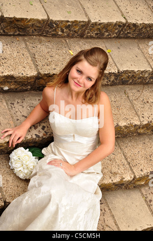 Eine attraktive weiße Braut sitzt im Freien auf Steinstufen. Stockfoto