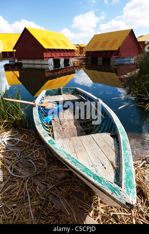 Den Nahverkehr auf den schwimmenden Inseln der Uros mit neuen Häusern im Hintergrund. Die Häuser waren ein Geschenk vom Staat. Stockfoto