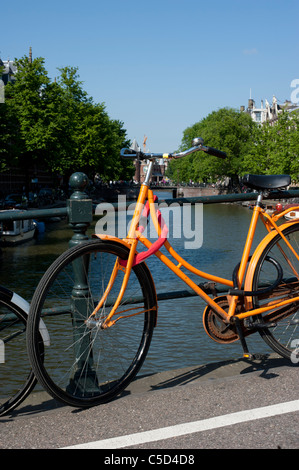 Orange Fahrrad angekettet an einer Brücke über einen Kanal in Amsterdam Stockfoto