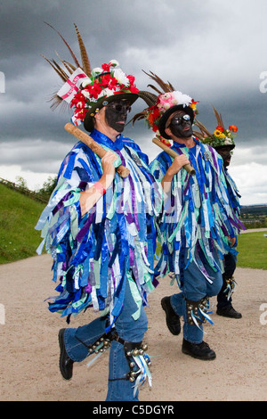 Exmoor Border Morris Tänzer, schwarz gesichtig, tragen lange fließende zerrissene alte Lumpen, Kleidung aus breiten Bolzen aus blauem und weißem Material, Kleidung & Tanzfeier, Outdoor-Veranstaltung, Street Dancer, kostümierte Tänzer, lange fließende Lumpen, Cloggies, führen, Leistung der Volksunterhalter, bunte Musiker, beliebt, Traditionelle Unterhaltung im Tutbury Castle Weekend of Dance Derbyshire, Großbritannien. Stockfoto